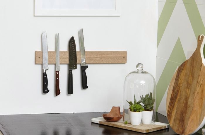A kitchen with a black benchtop and knives on a magnetic rack on the wall
