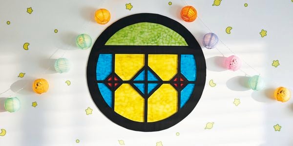 A round stained glass-look window made from black flute board with coloured cellophane as the panes, attached to a wall with paper lanterns and glow in the dark stickers