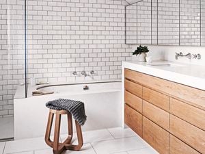 A bathroom with white tiles, a wooden vanity and a wooden stool.