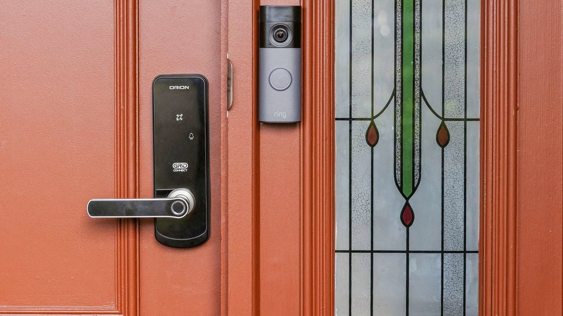 Smart door lock and Ring video doorbell installed on a red front door with decorative glass panel
