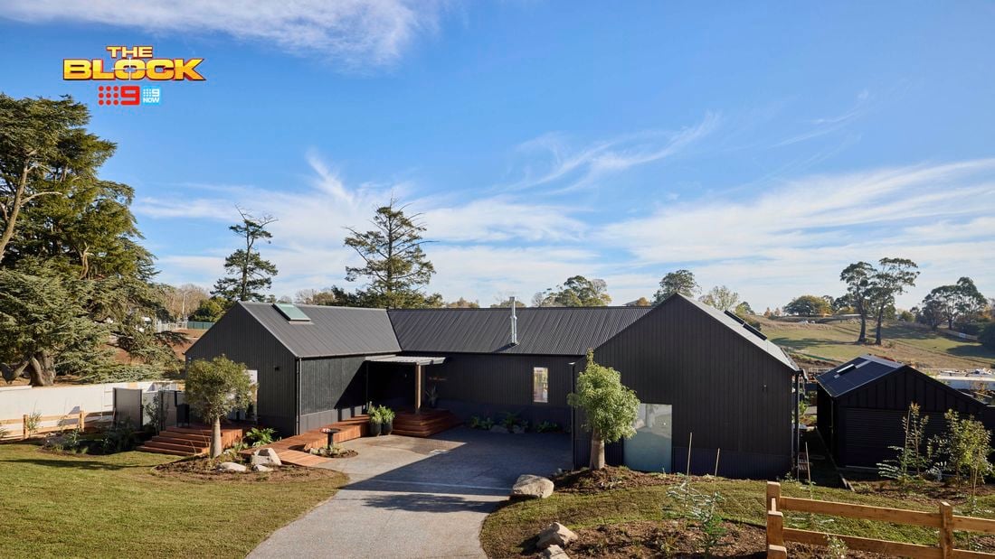 The front of a house with a driveway in it, trees, and a timber fence.