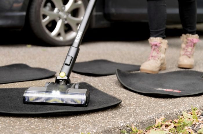 A person is using an illuminated light vacuum cleaner to clean car floor mats.]