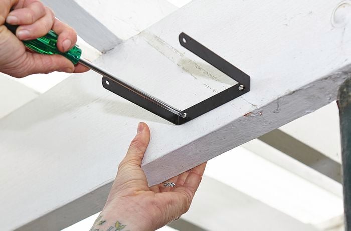 A person attaching a metal bracket to the beam of a pergola