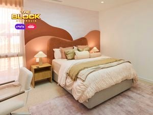 Cream bedroom with a queen bed, desk and mirror on a blush rug and a red and orange hill style bedhead.