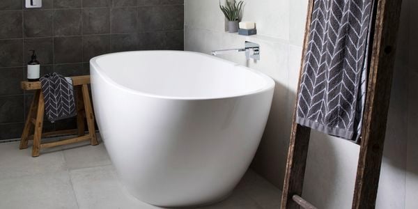 Grey and black tiled bathroom with white bathtub and towel hanging on rustic ladder.