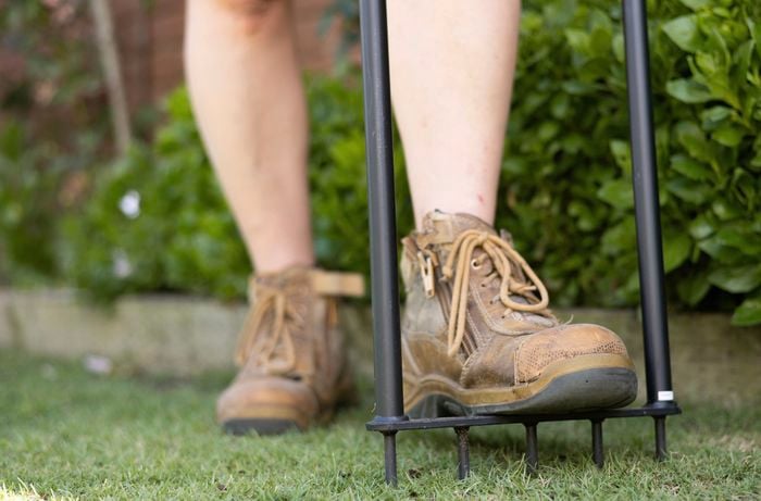 A person is poking tiny holes into the soil using a lawn aerator