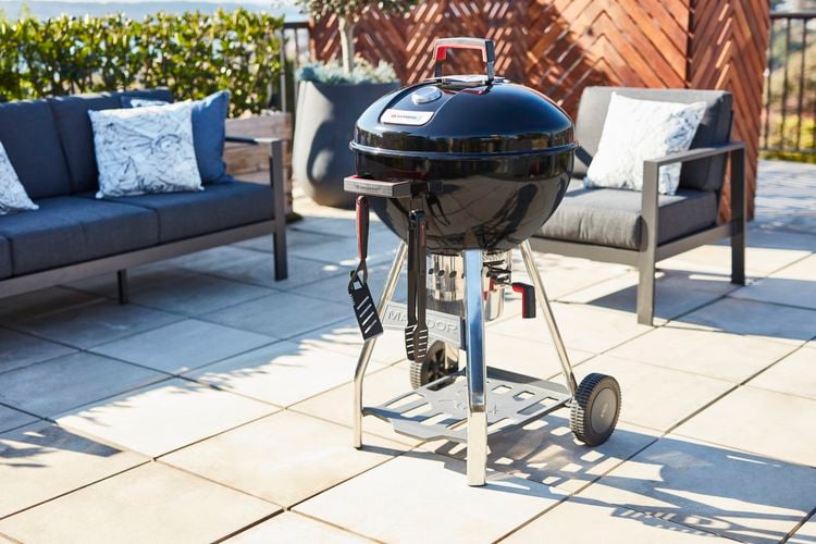 Kettle barbecue in a backyard next to an outdoor lounge
