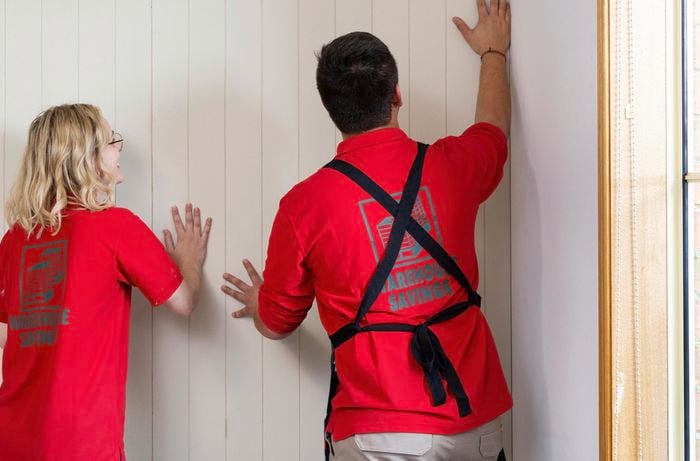 Two people putting VJ feature wall panel in place, against a wall.