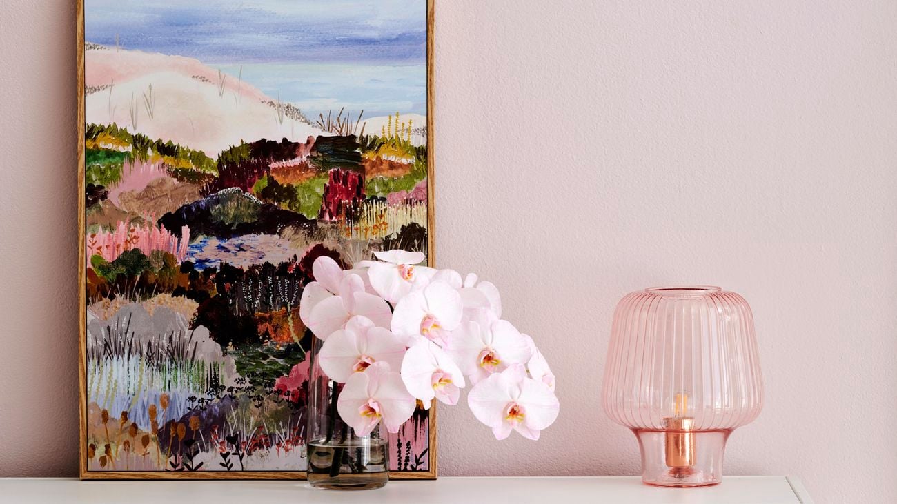 Shot of cabinet with pink flowers and a pink glass lamp in foreground and a painting in background.