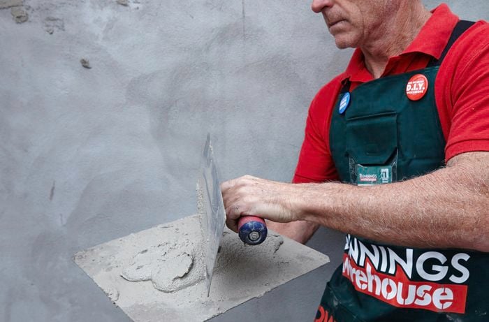 A Bunnings team member mixing render on a hawk before applying it to a wall