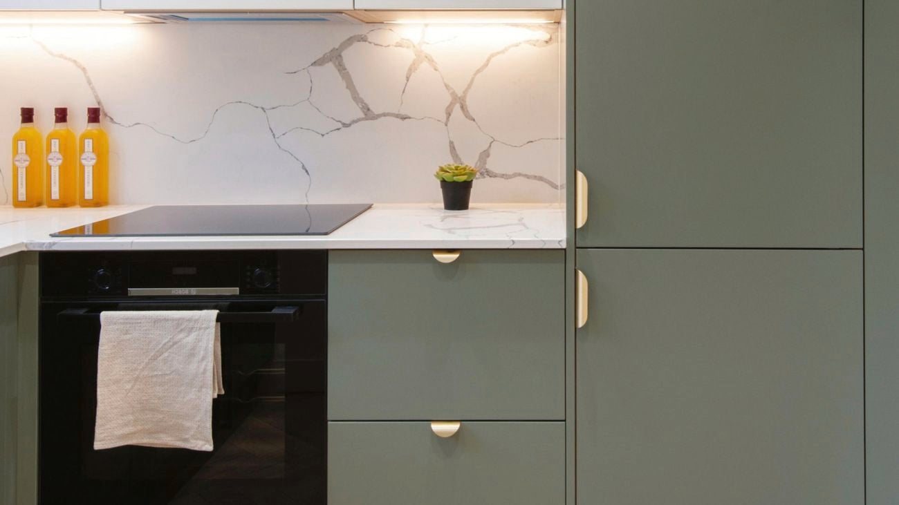 Kitchen with green cupboards attached to an oven with stove light turned on