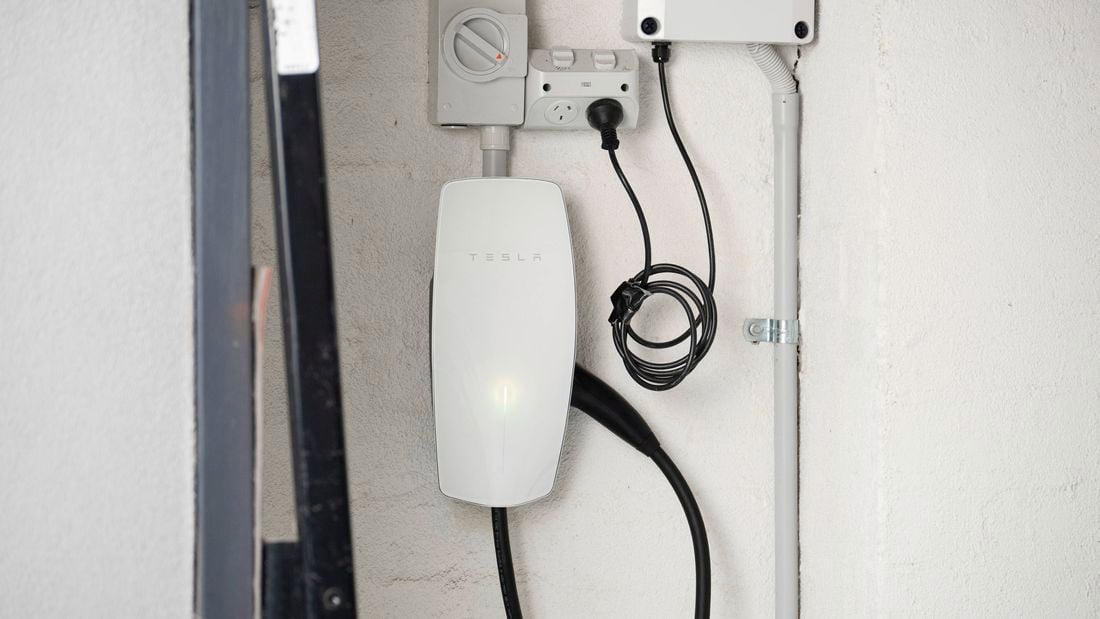 A Tesla Wall Connector is mounted on a wall, neatly installed with connected power cables. 