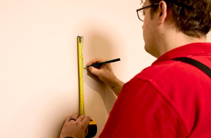 A Bunnings Team Member holding a tape measure and a pencil against a wall