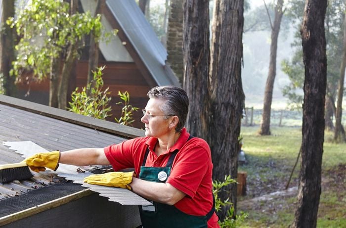 Person sweeping leaves off a corrugated roof in a bushland setting