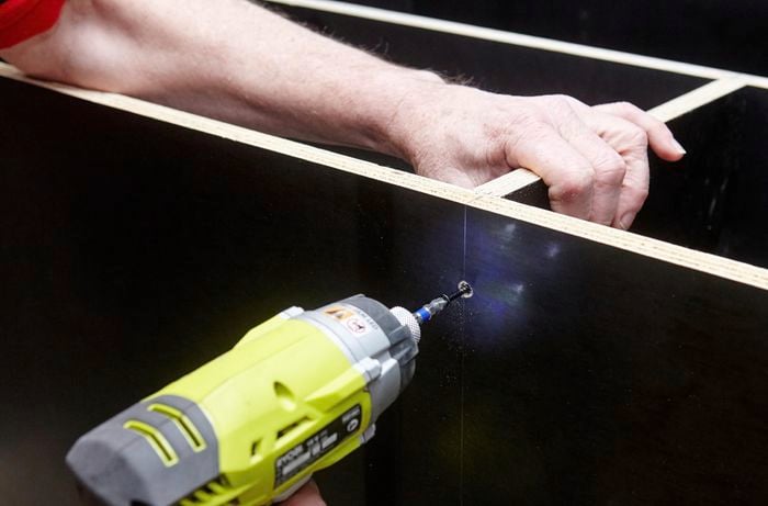 Person drilling nail into cabinet divider