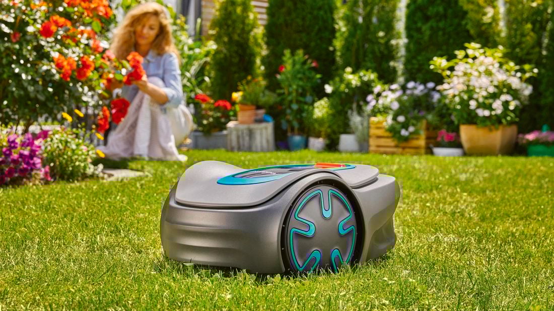 Gardena robotic lawn mower on the lawn with woman in background pruning roses