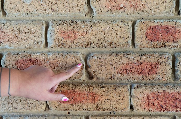 Person inspecting mortar joint on brick wall