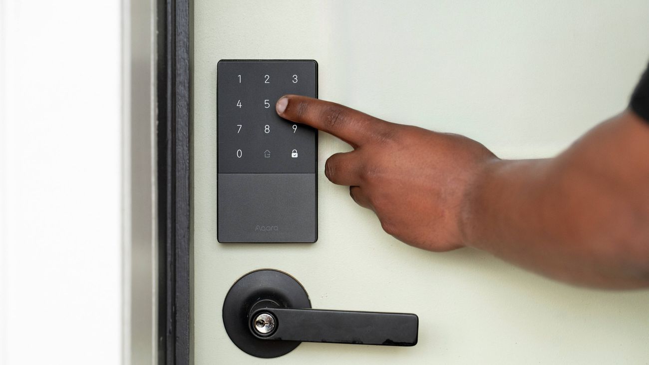 Close-up of a person entering a code on a smart keypad door lock mounted above a black door handle on a front door.