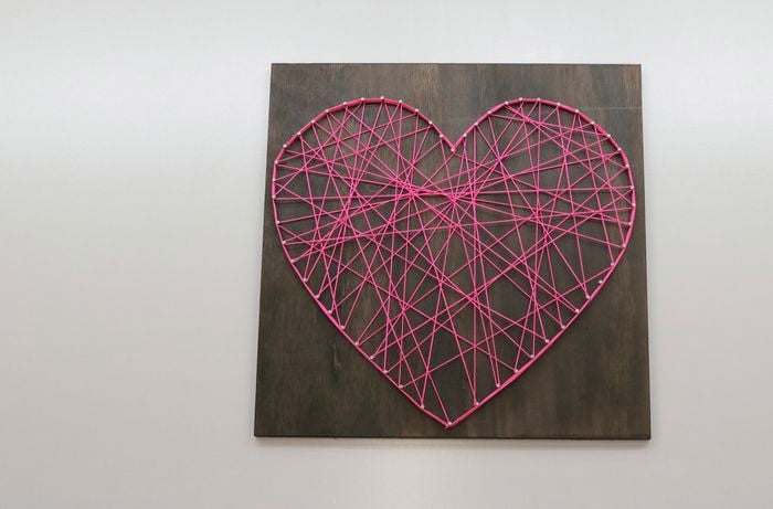 Heart shape made of pink string on stained wood