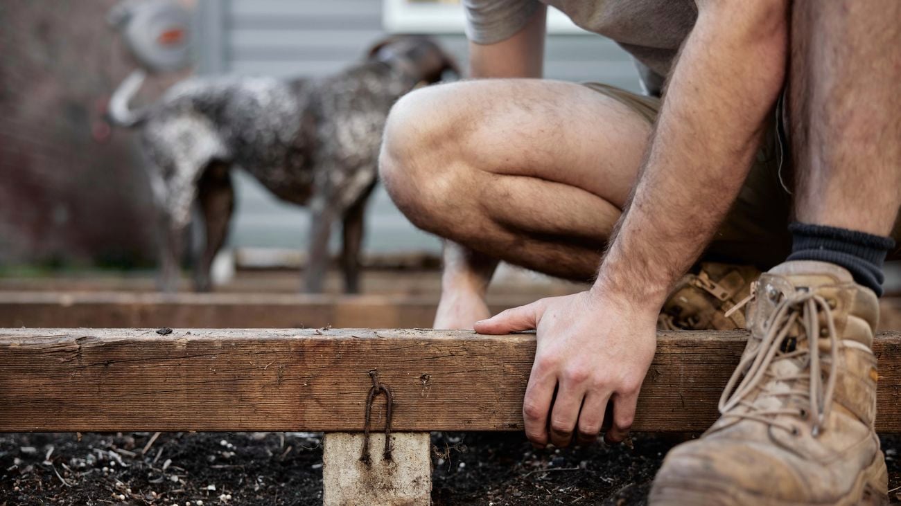 Hands on two planks of wood, slightly raised, attached to each other at a 90 degree angle 