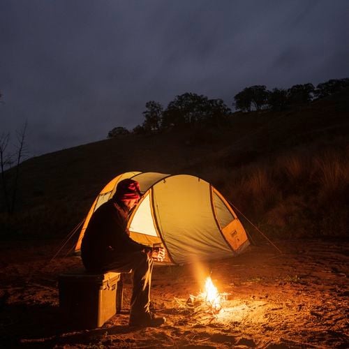 Man sitting by fire with view of tent in the background.