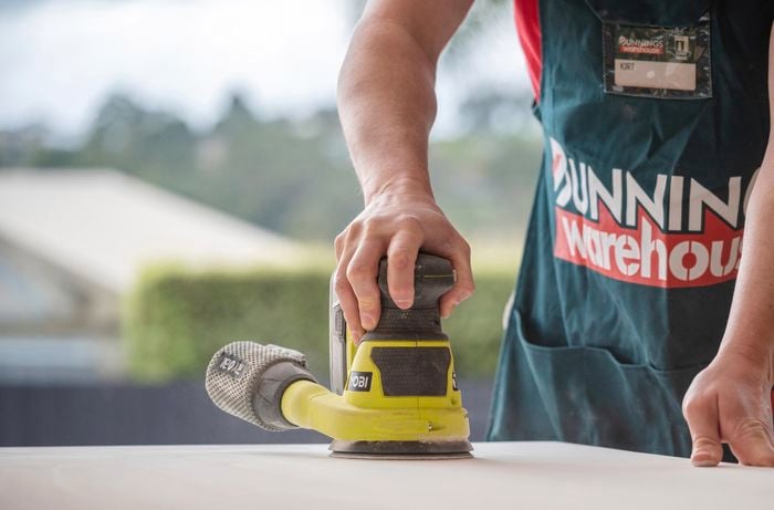 A person sanding both front and back of a door using an orbital sander.