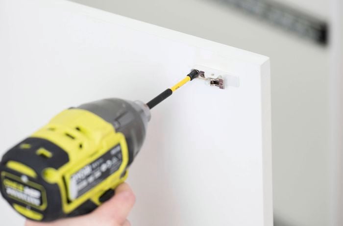 A person is using a power drill to insert the hinge cup into the pre-drilled recess on the door