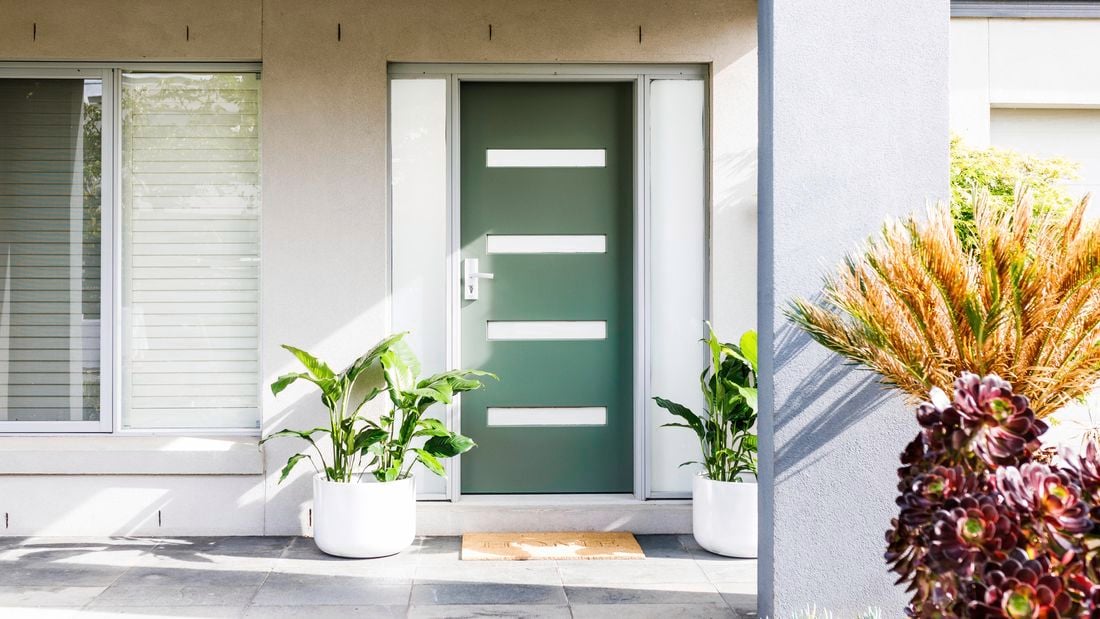 Freshly painted green front door with two potted plants either side.