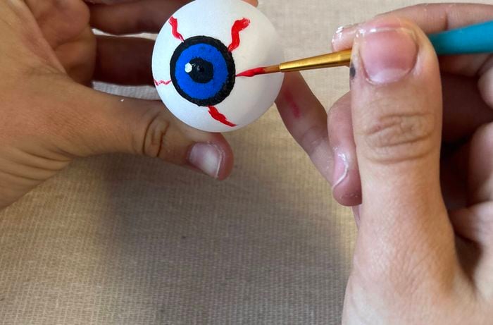 Red veins are painted onto a ping-pong eyeball with a small artist’s brush