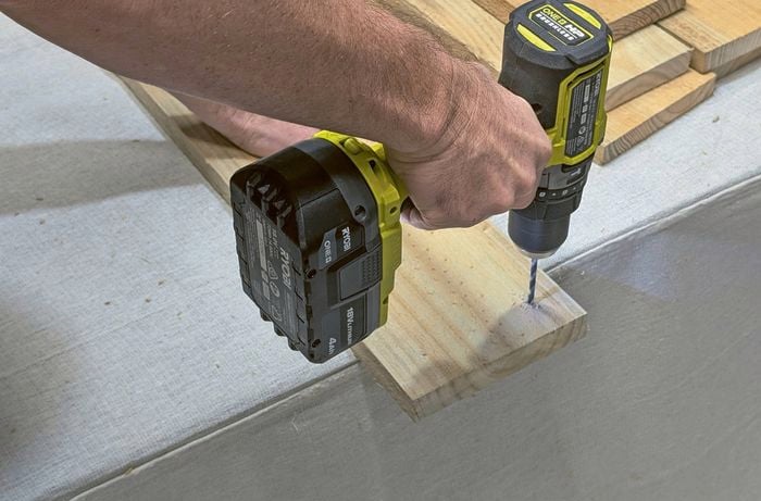 Hands using a drill to predrill a hole in a piece of timber.