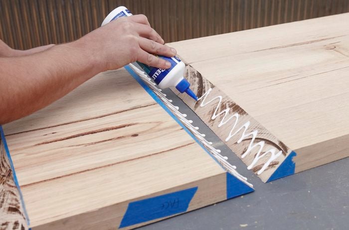 A person applying glue to the mitred ends of two pieces of hardwood