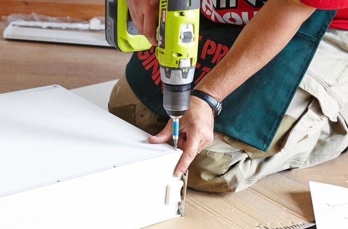 A person attaching a drawer base using a cordless drill