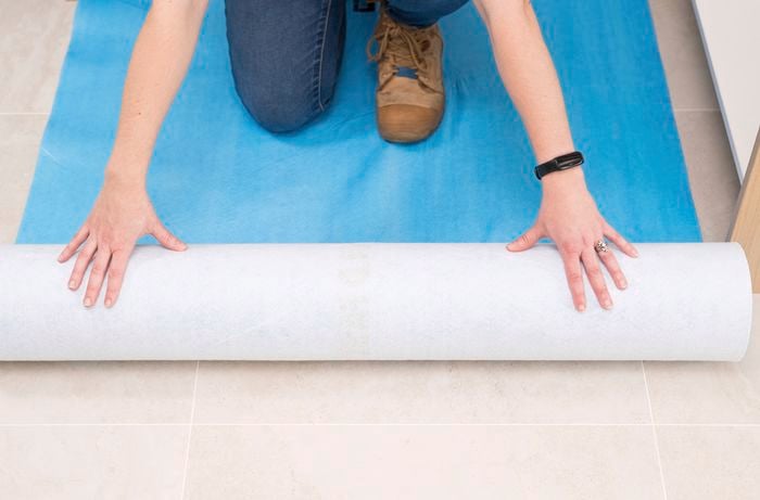 A person is laying a drop sheet to protect the floor from scuffs, scratches, and damage during work.