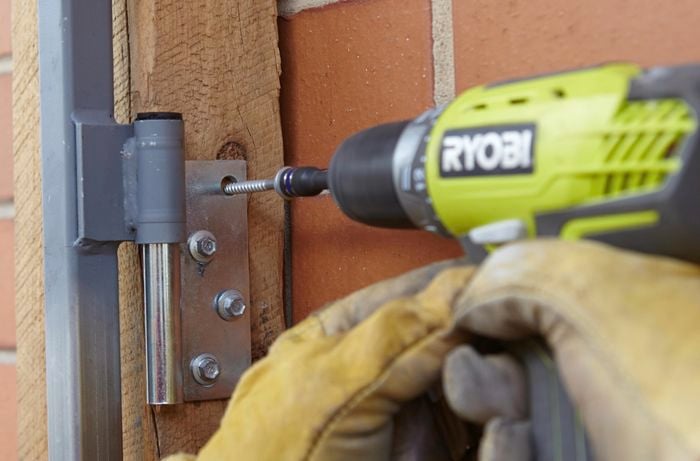 A person attaching a gate hinge to timber post using a cordless driver