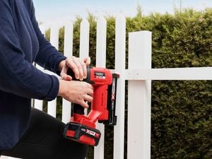 A man wearing a protective safety mask uses a paint spray gun to spray light blue paint onto a white fence.