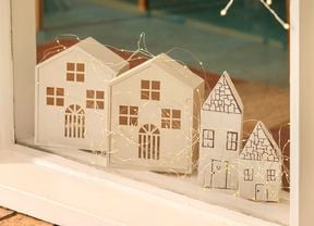 A windowsill display featuring four small white timber houses decorated with string lights.