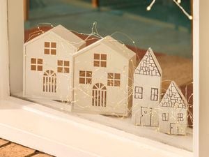 A windowsill display featuring four small white timber houses decorated with string lights.