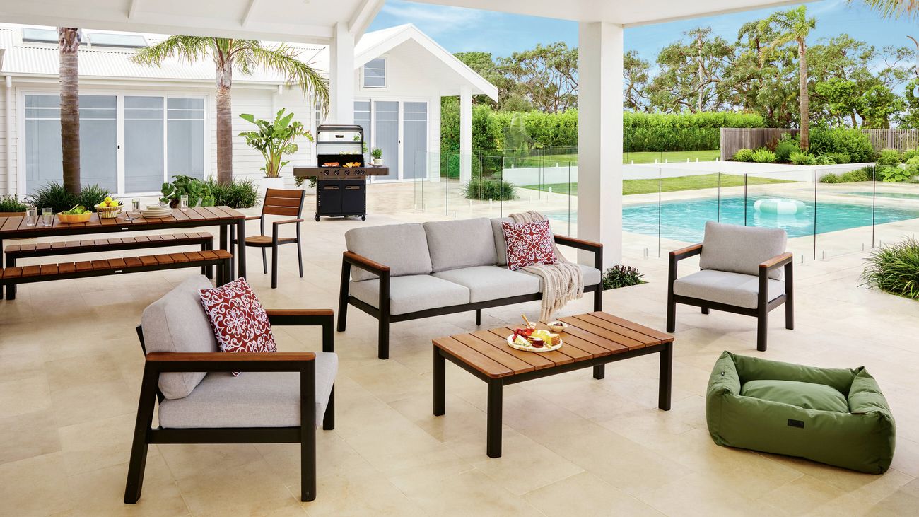 Covered outdoor entertaining area featuring cushioned lounge seating, a timber coffee table, barbecue and swimming pool.