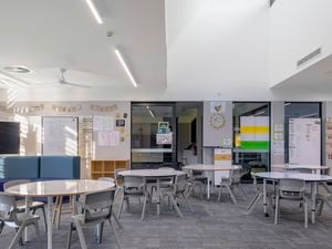 Modern classroom with round tables, chairs, large windows, and educational posters on the walls.