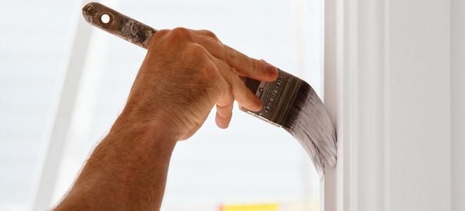 Close up of a hand painting an interior timber moulding with white paint
