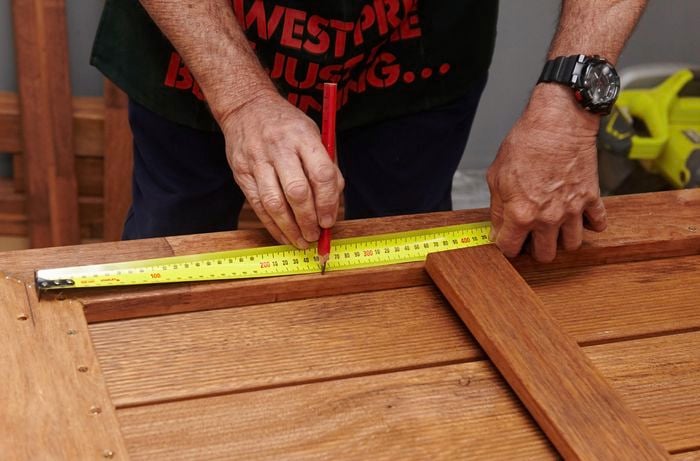 Person using measuring tape and making a mark on piece of timber.