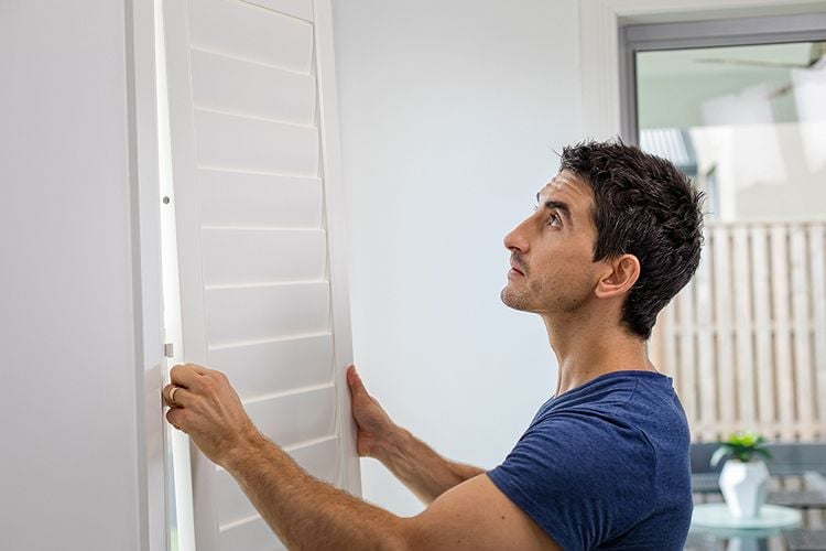 A tradesman fitting blinds to a window frame