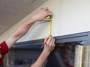 Person marking an exterior wall above a window using a measuring tape and pencil