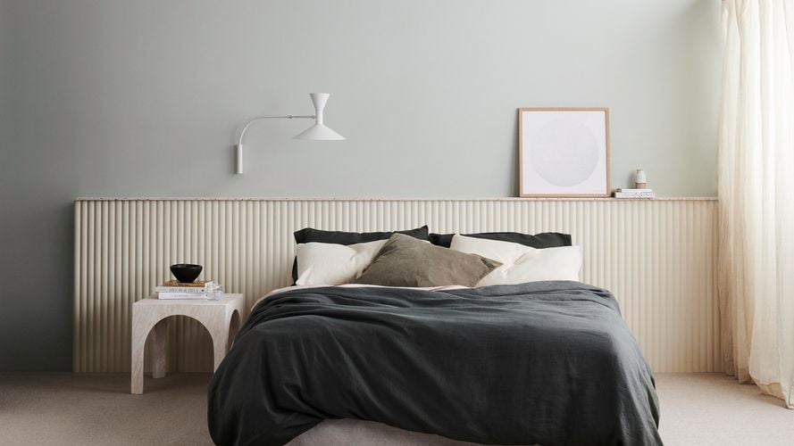 Bedroom with bed, scattered pillows, side table with books, mounted lamp and print. Demi Round 40 design.