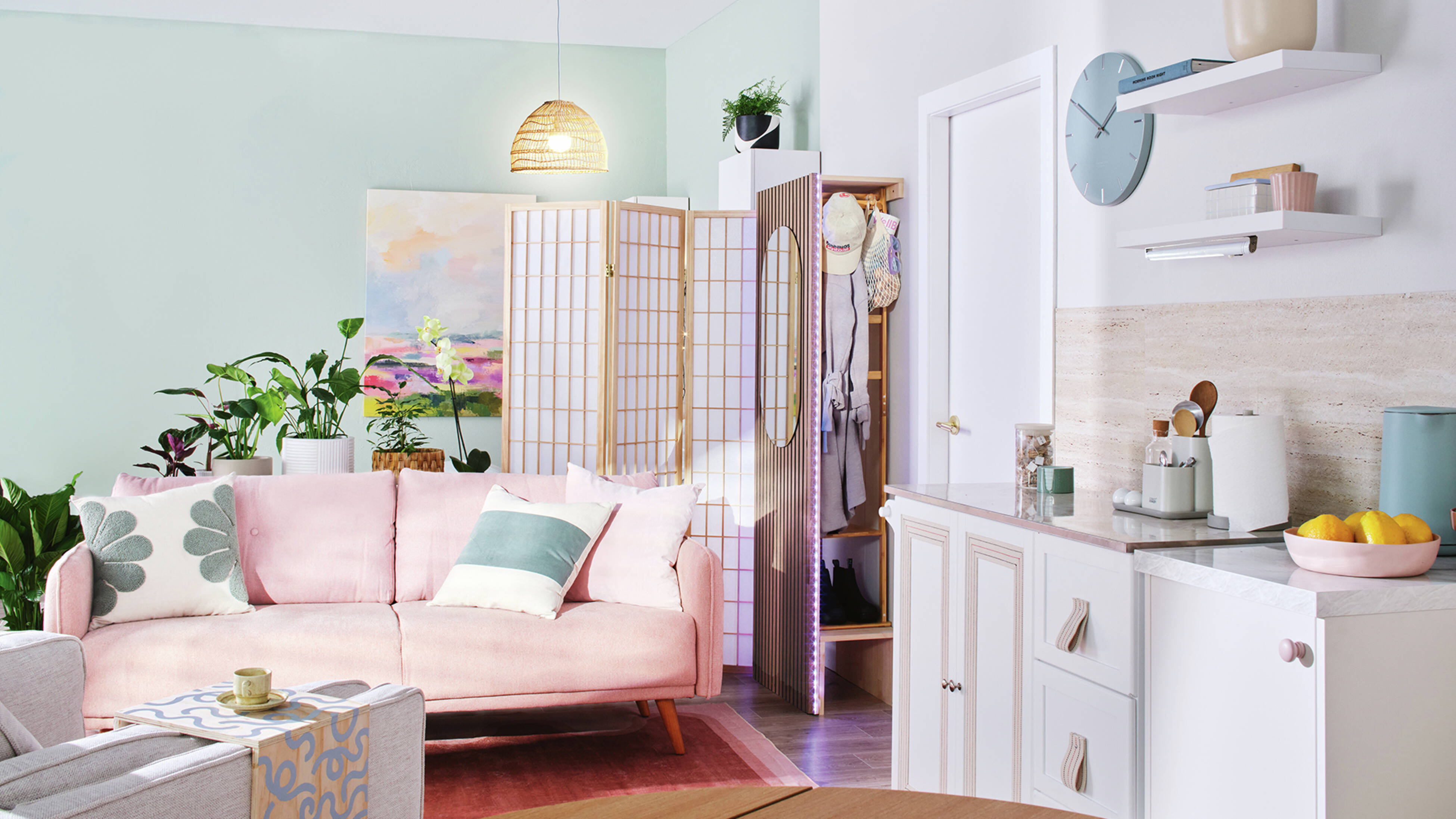  The corner of a kitchen and lounge area with a pale pink lounge, room divider and mini cloakroom.