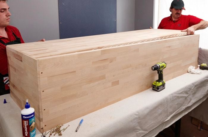 Two people placing base of modern timber sofa lounge down.