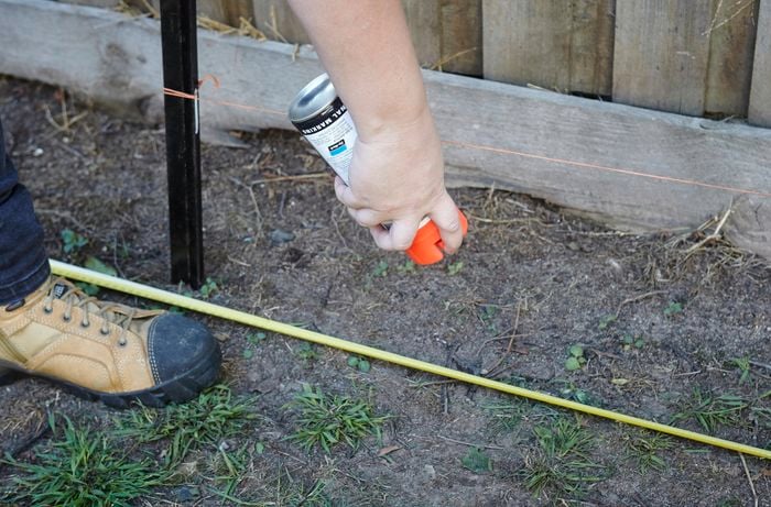 A person marking the ground with spray paint underneath a string line