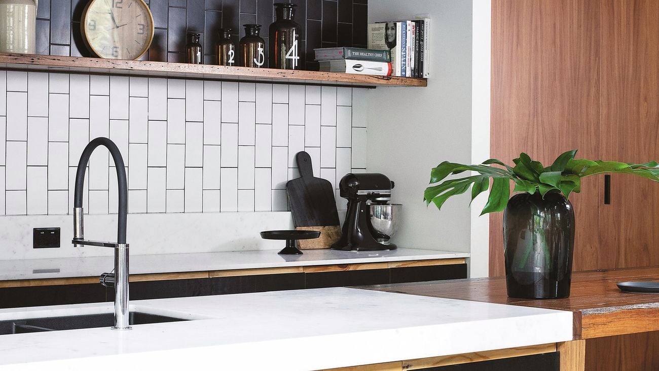 Modern kitchen with black and white subway tile splashback, black cabinetry, white benchtop and stainless steel tap.
