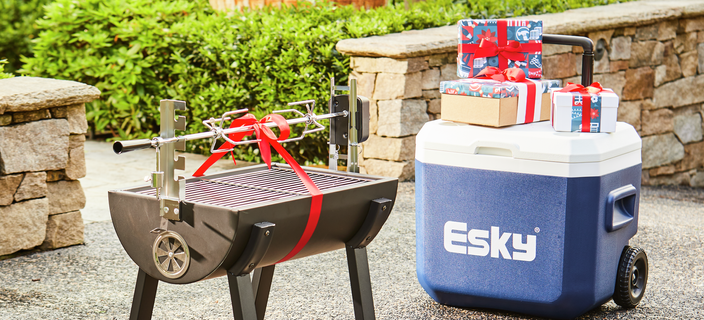 A spit roaster and an esky with Christmas presents and bows are outside in a garden.