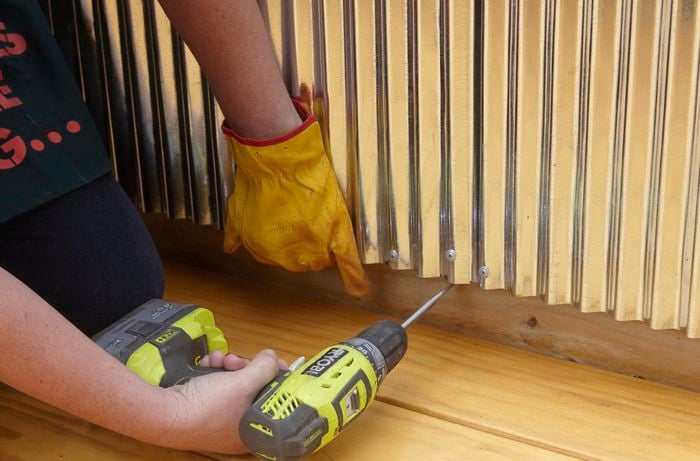 Person drilling into timber underneath metal sheet feature wall.